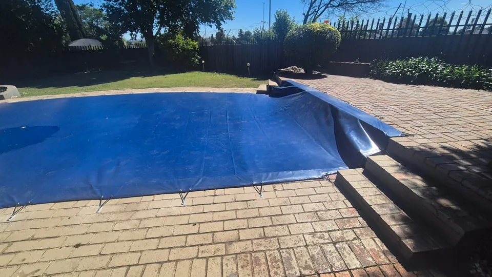 Blue solid cover shaped up and around a raised paved pool edge and adjacent steps