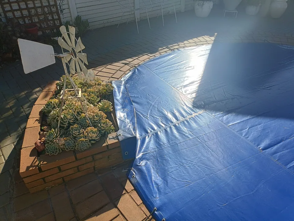 Closer view of the blue cover shaped around the raised brick planter with visible eyelets and fixings