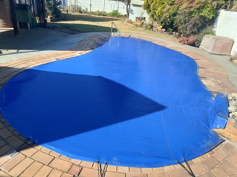 Full view of a blue cover on a curved pool with a raised planter and existing handrail