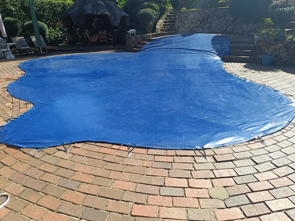 Blue custom-shaped cover following curves and an elevated pool section beside stonework