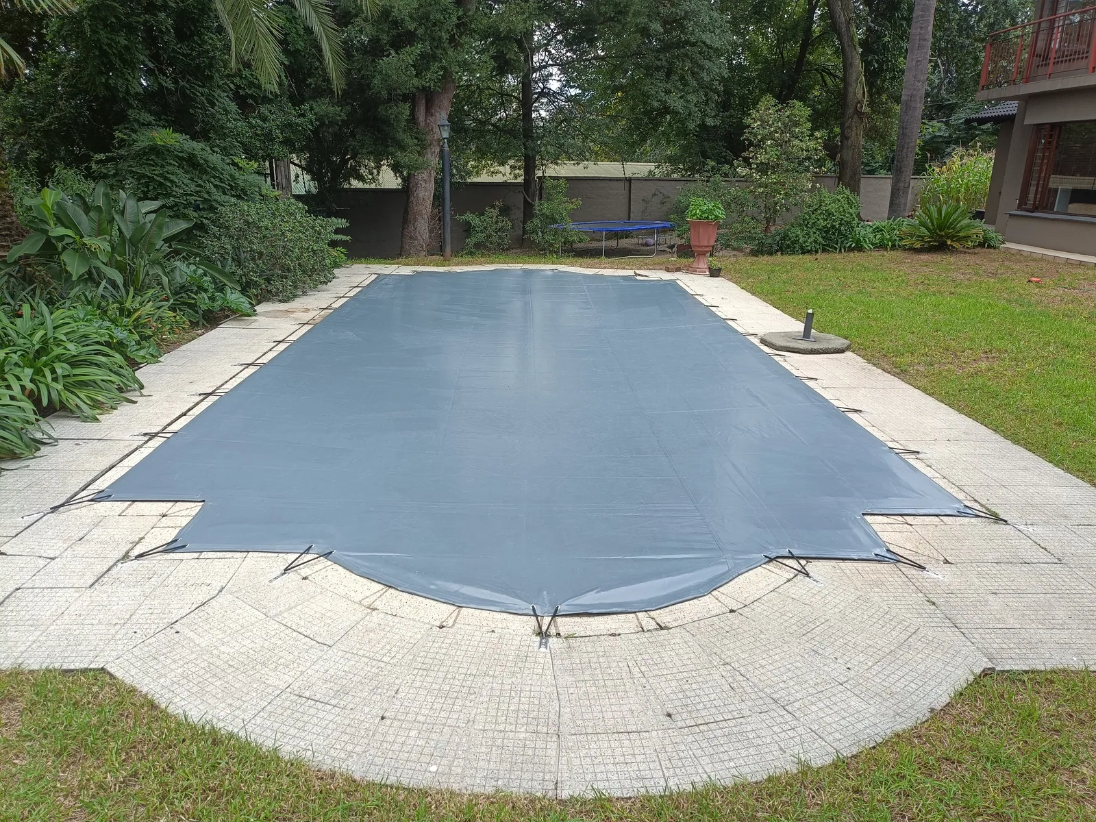 Grey solid pool cover following the stepped and curved outline of a garden pool
