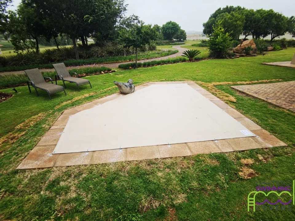 Light solid cover fitted with perimeter hooks and plates in a landscaped garden